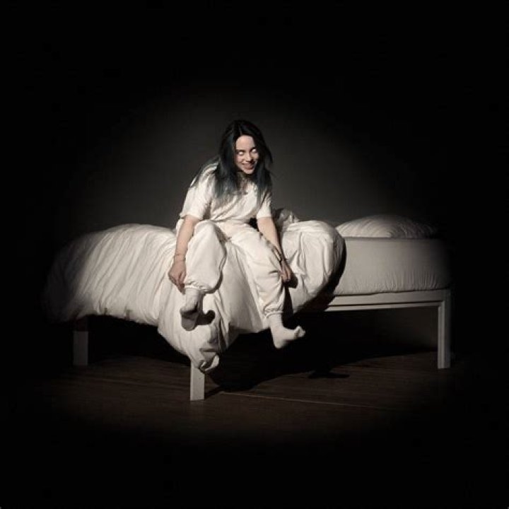 Billie lying on a bed (headshot) with her hands shown, every finger filled with rings. Her Net Worth is helping her.
