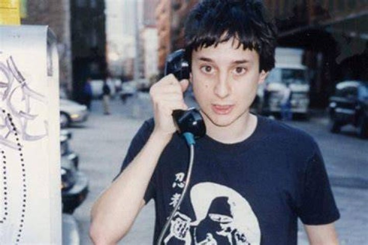 Harmony Korine has his eyes covered by his hands and his trident tattoo is visible on his right hand.