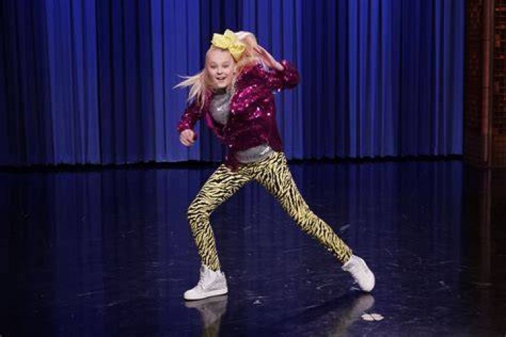 JoJo Siwa jumping up in the air with a mic stand in her hand.